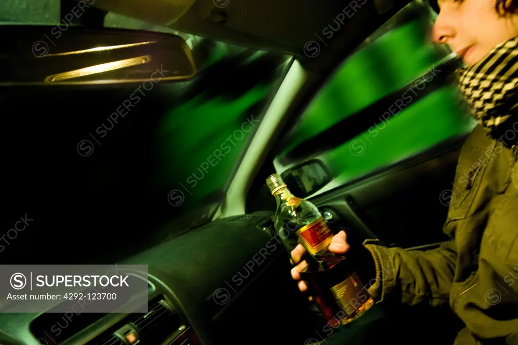 Teenage boy  with whisky bottle sitting in car