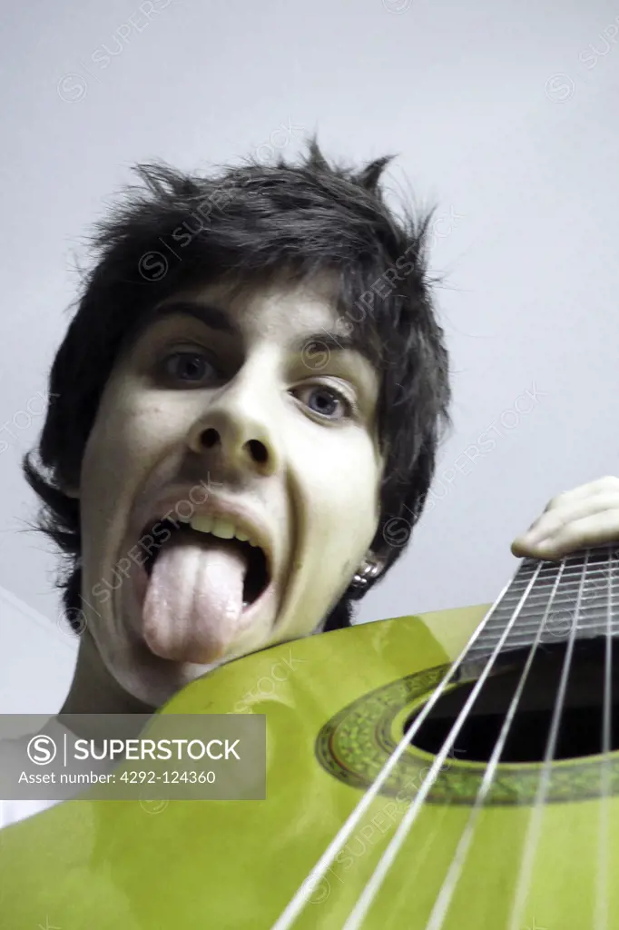 Portrait of teenage boy with guitar sticking out tongue