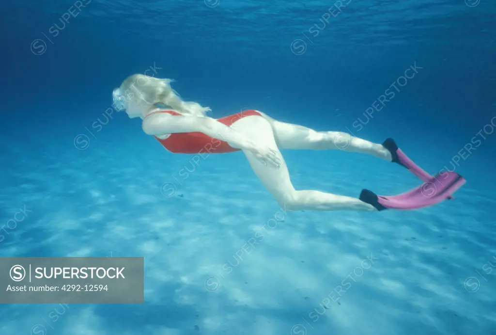 Young blond hair woman swimming underwater with flippers, underwater view