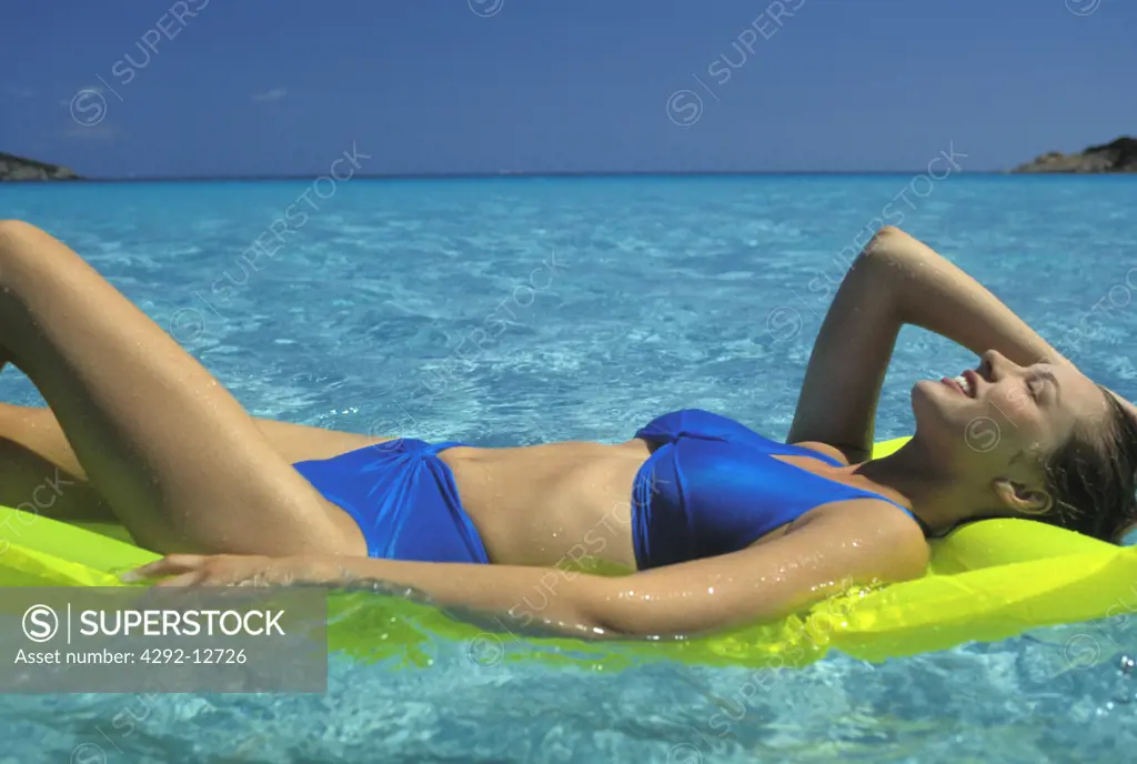 Smiling woman lying on an airbed in sea water, sunbathing, relaxing.