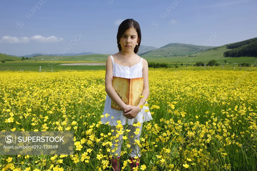 Girl standing in buttercups field holding book
