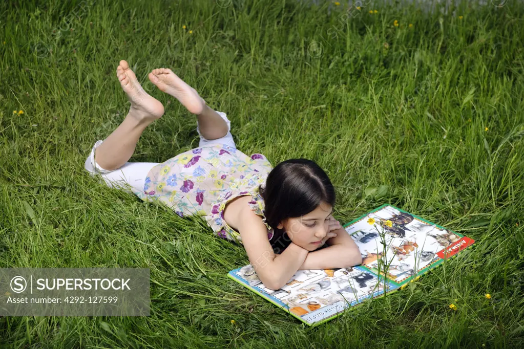 Girl lying on grass reading book
