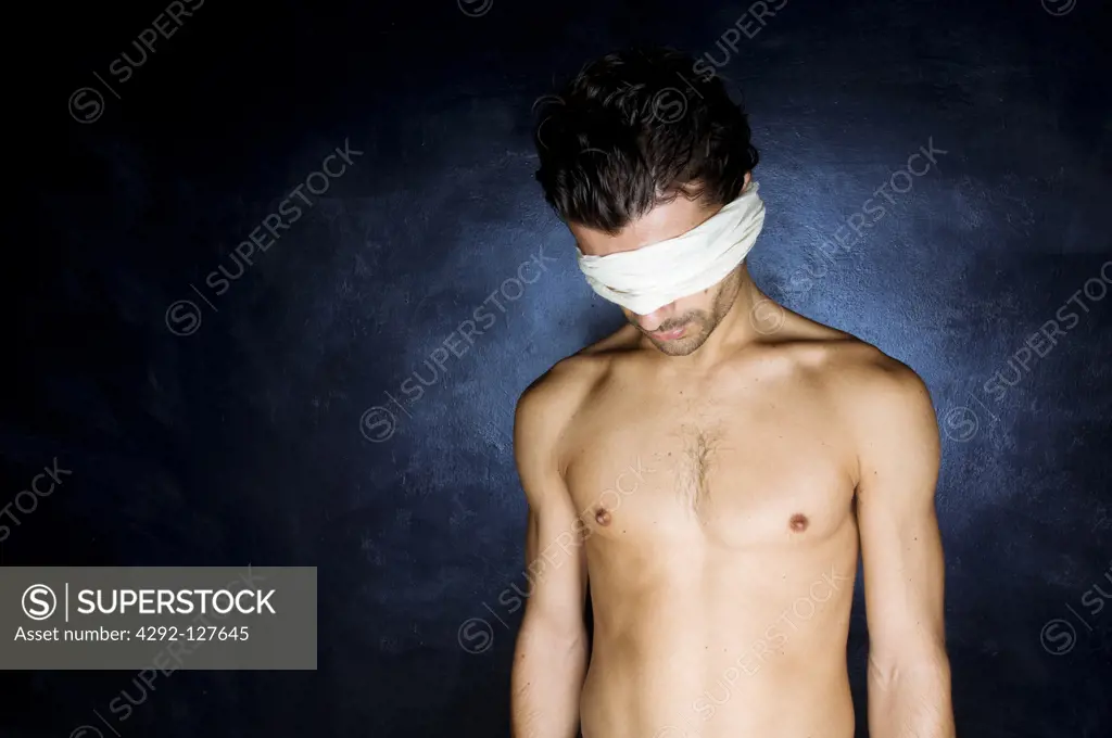 Portrait of blindfolded young man standing on dark blue background