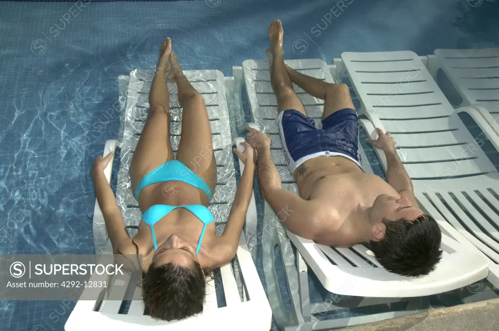 Couple in swimsuit lying on deckchair in a swimmingpool