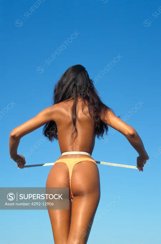 Rear view of a woman with thong measuring her waist