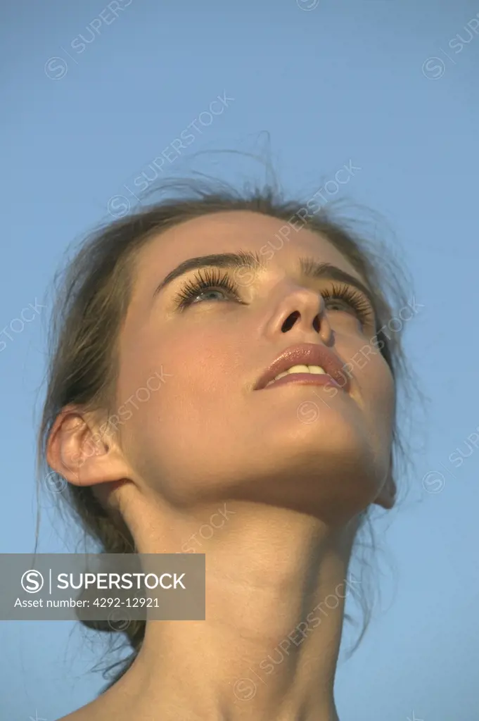 Portrait close up of the face of a serious young woman outdoor, looking up at blue sky
