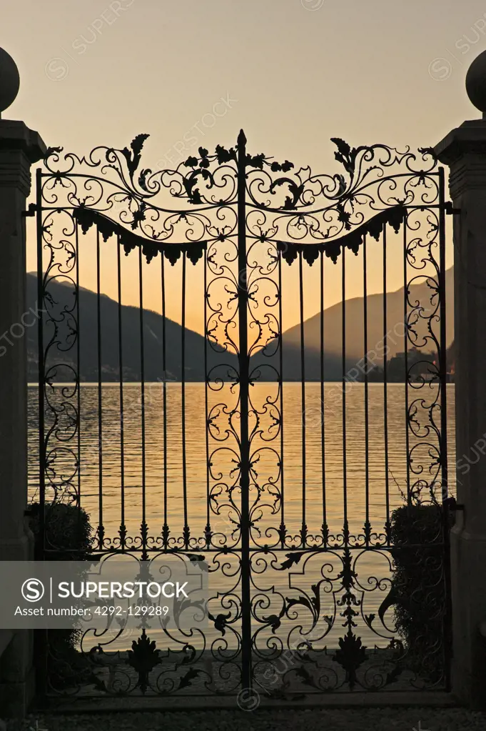 Switzerland, Ticino Canton, Lugano, Gate in a garden infront Lake at Sunset