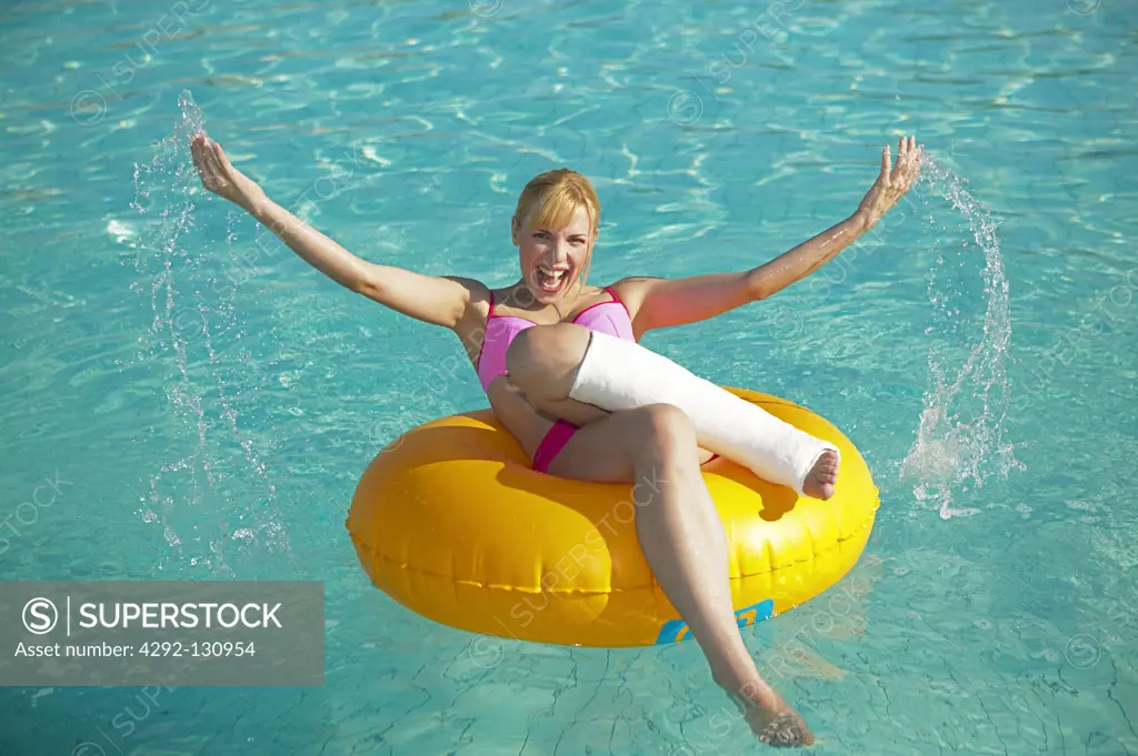 Frau mit Gipsbein auf Gummireifen im Pool, woman with leg in cast on a rubber tyre in the pool