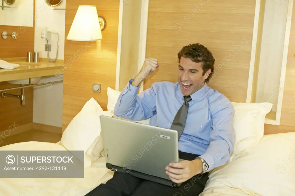 Manager arbeitet mit dem Laptop in seinem Hotelzimmer, Happy Manager working on a laptop in his hotel room