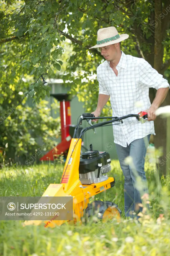 Mann maeht das Gras in seinem Garten mit einem Balkenmaeher