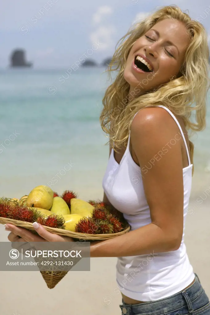 young blond woman on beach with tropical fruits in portrait