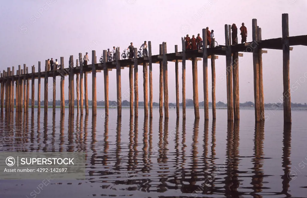 Myanmar, Amarapura, monks cross the U-Bein bridge at dusk . The bridge is the longest teak one in the world, 1, 2 km