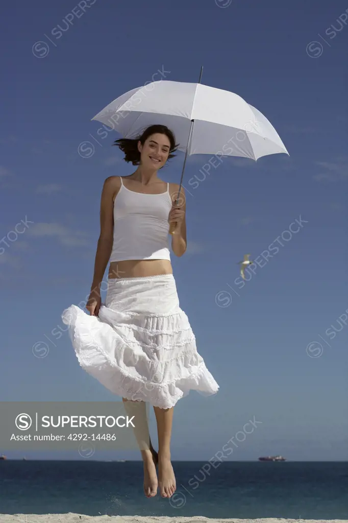 Jumping woman on beach with parasol