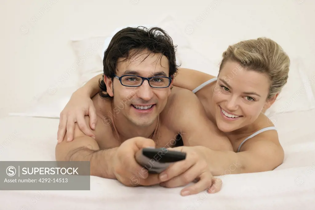 Couple lying on bed with remote control