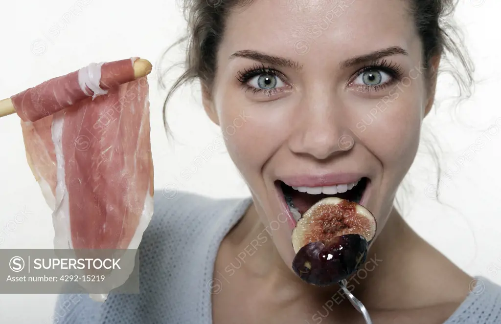 Woman eating fig and , view on the right of her a breadstick with ham
