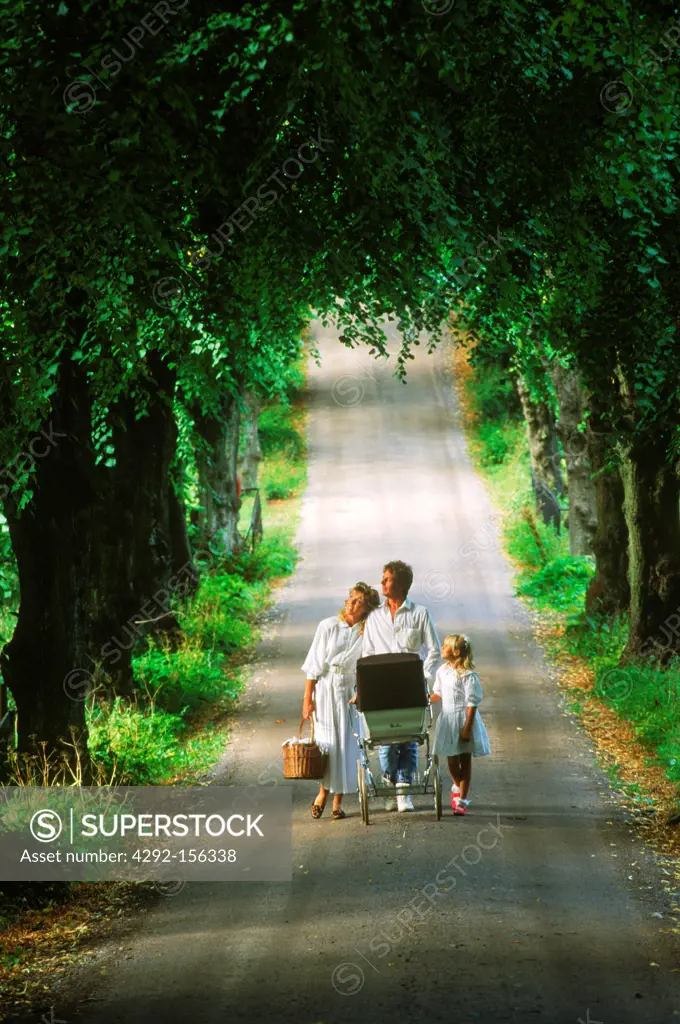 Family of four with baby stroller on tree lined country road in Sweden