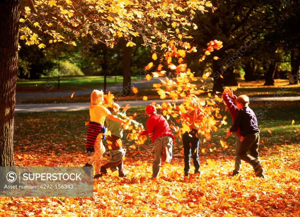 Kids tossing autumn leaves in Royal National City Park called Haga Park in Stockholm