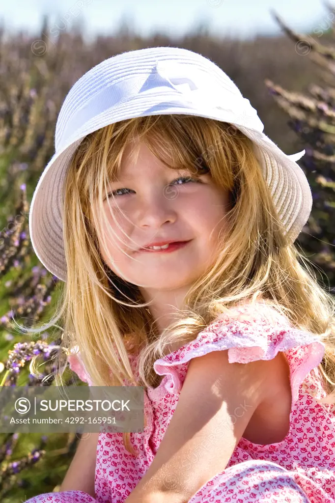 little girl sitting into a lavender field wearing a white straw hat