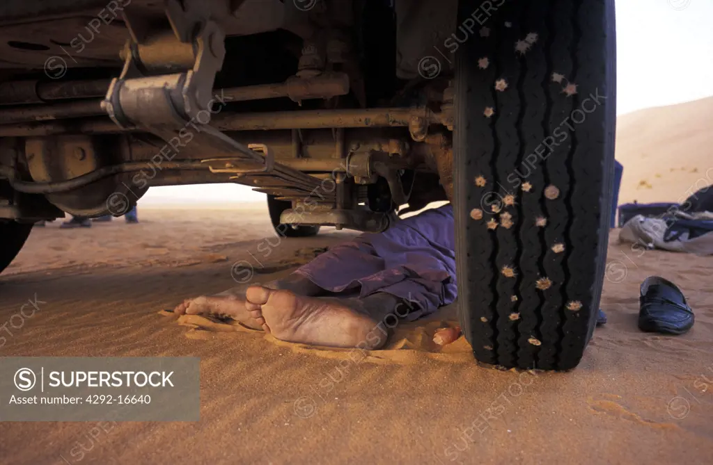 Algeria, Sahara, Erg Chech Desert, feet of a person lying under a car in the desert