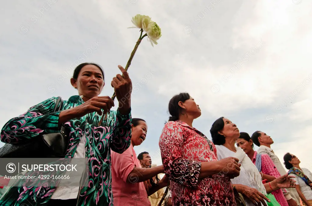 Cambodian people hold lotus flowers as they pray at a shrine in front of the Royal Palace in Phnom Penh