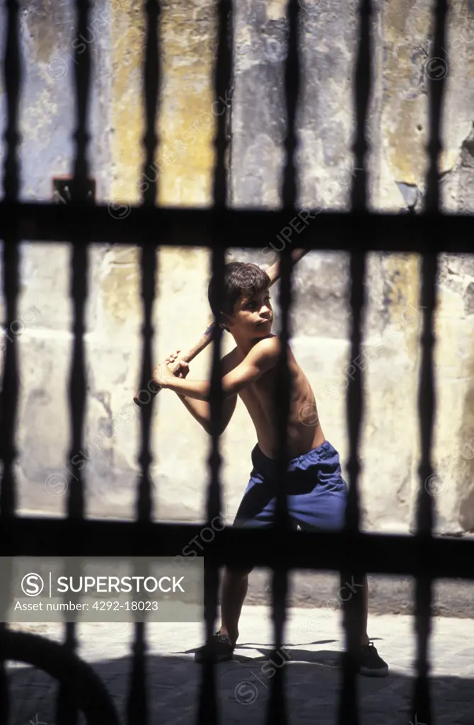 Cuba, Santiago de Cuba: boy playing in the street behind a fence
