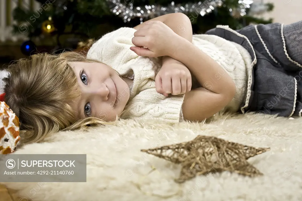 girl laying on white rug near Christmas tree