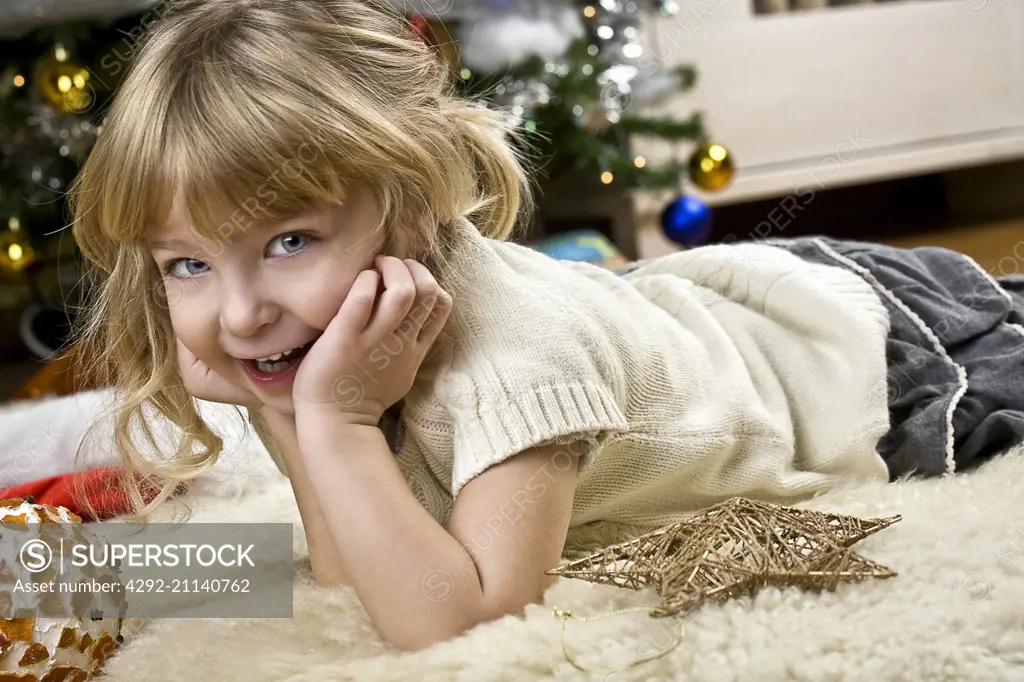 girl laying on white rug near Christmas tree