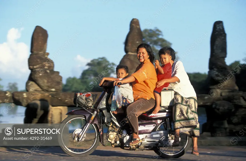 Cambodians on motorcycle in front of old statues of a temple