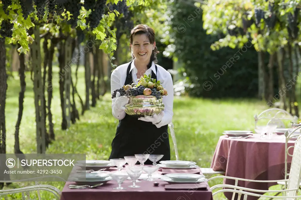 Italy, Veneto, Pedemonte,waitress setting table for party in the vineyards of the Hotel Villa del Quar