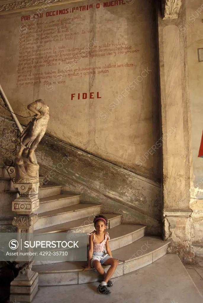 Cuba, Havana, Old town. Girl sitting on stairs under statement of Castro
