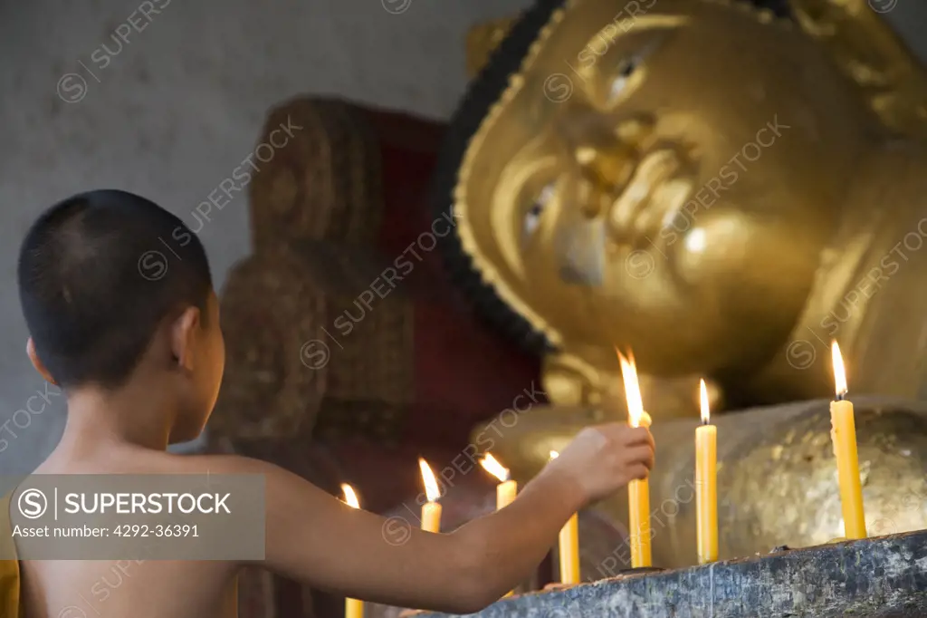 Thailand, Chiang Mai, Young Buddhist Monk lighting candle at Buddha statue in temple Wat Chedi Luang (no property release)