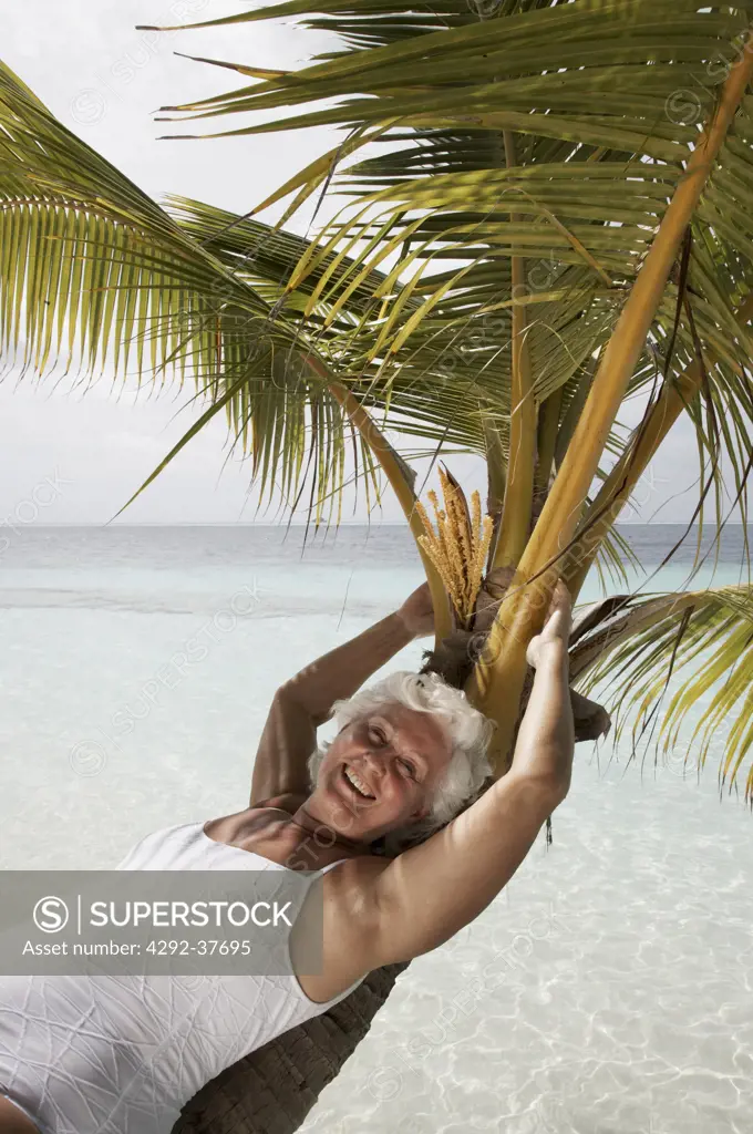 Maldives, Ari Atoll, senior woman lying on a palm tree