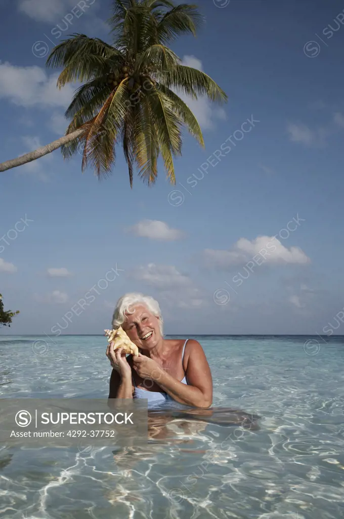 Maldives, Ari Atoll, senior woman listening to a sea shell