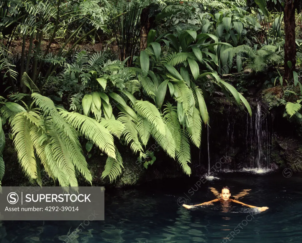 Woman swimming in a pond with waterfall and tropical plants