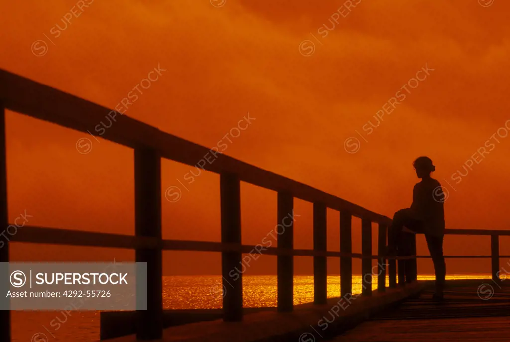 Silhouette on a boardwalk by the ocean at sunset