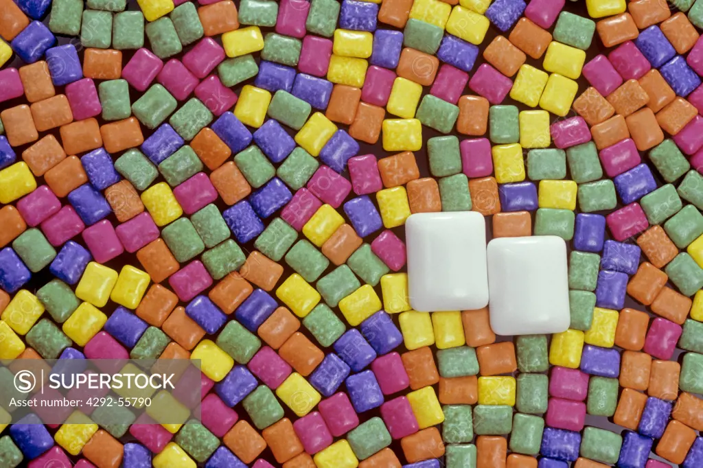 Tiny pieces of candy coated chewing gum in a rainbow pattern surrounding two white pieces of gum