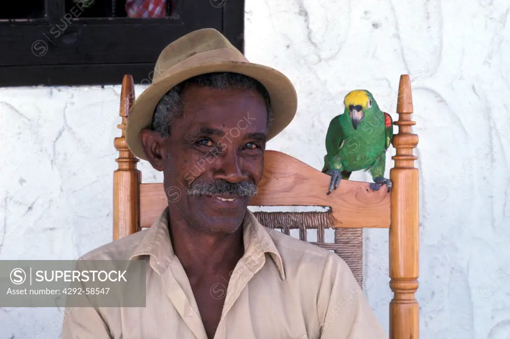 Antilles, Curacao, Mature african man sitting on porch with parrot on shoulder