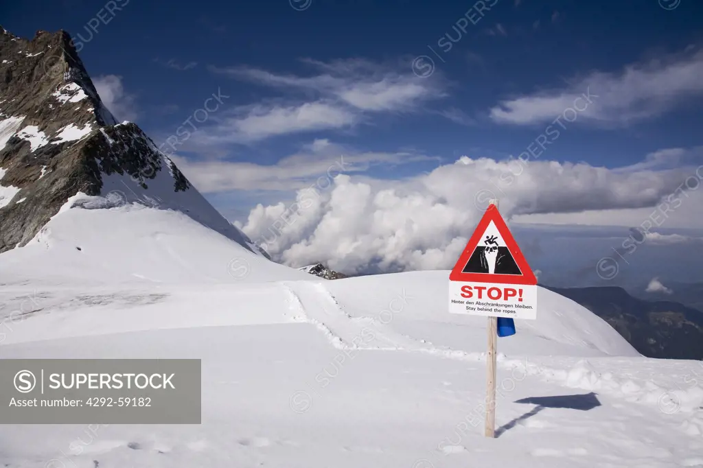 Danger sign behind rope barrier warns of glacier crevasse and Alps mountain view from the Jungsfraujoch