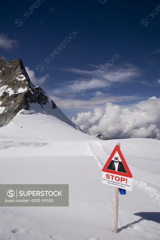 Danger sign behind rope barrier warns of glacier crevasse and Alps mountain view from the Jungsfraujoch