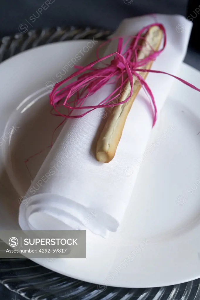 Folded napking with ribbon and breadstick on plate