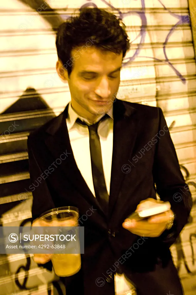 Italy, Lombardy, Milan, young man outside with cocktail and mobile