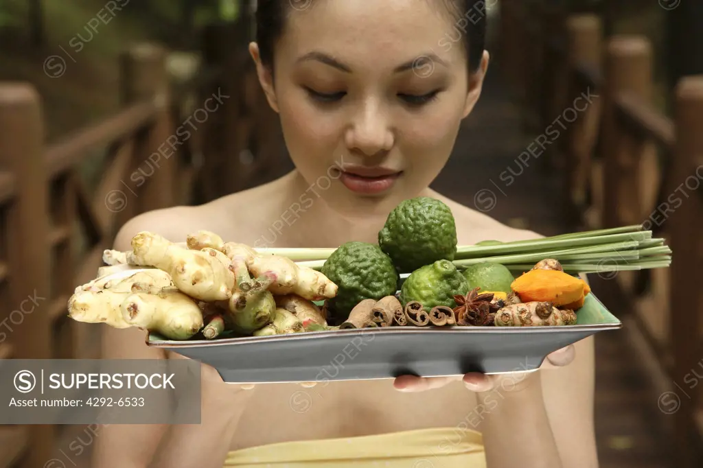 Girl holding a tray full of ingredients for Jamu - Indonesian Herbal Elixir