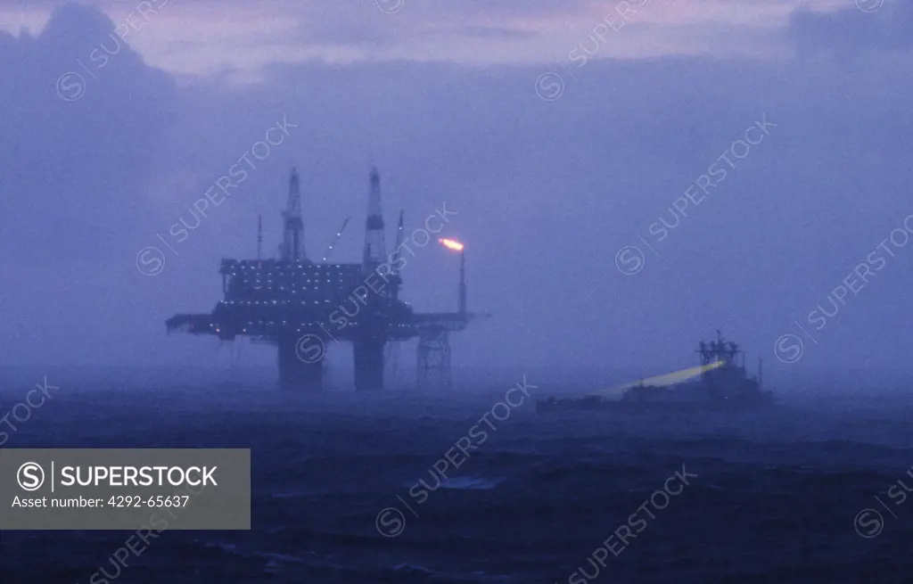 Oil production platform and safety boat during rain storm, North Sea