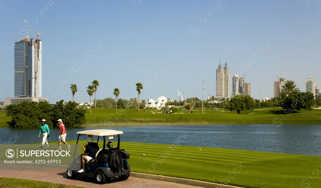 United Arab Emirates, Dubai, Golfers and buggy on Emirates Golf Course, Club House in the background and new buildings on Sheikh Zayed Road.