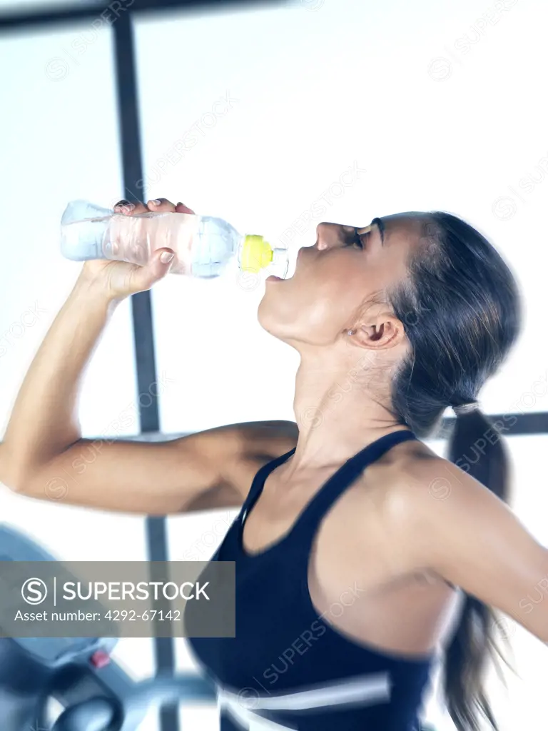 Young woman in fitness room drinking water from a bottle