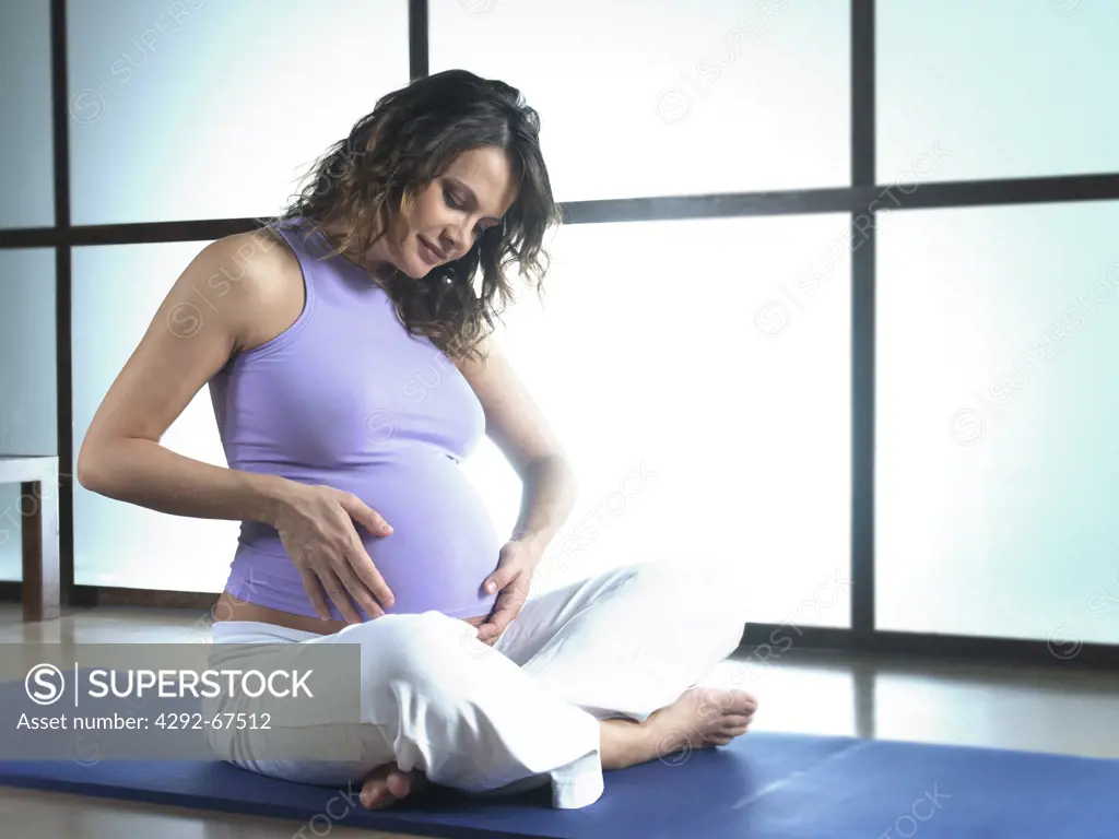 Pregnant woman sitting on exercise mat touching her belly