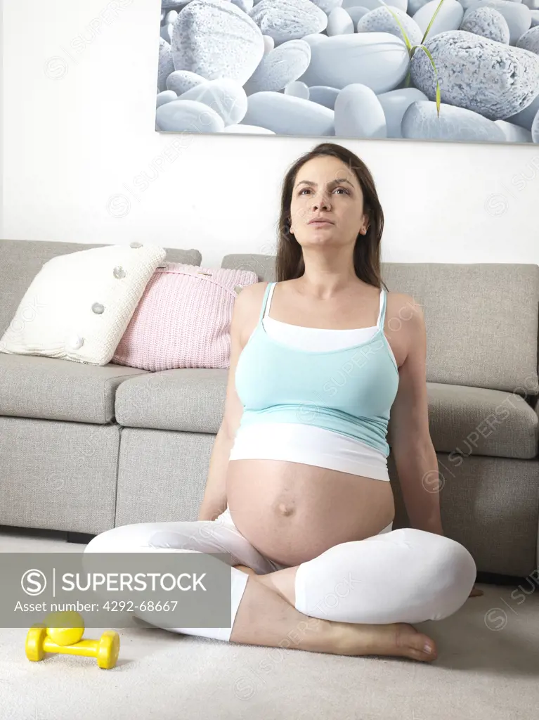 Pregnant woman with legs crossed exercising in livingroom