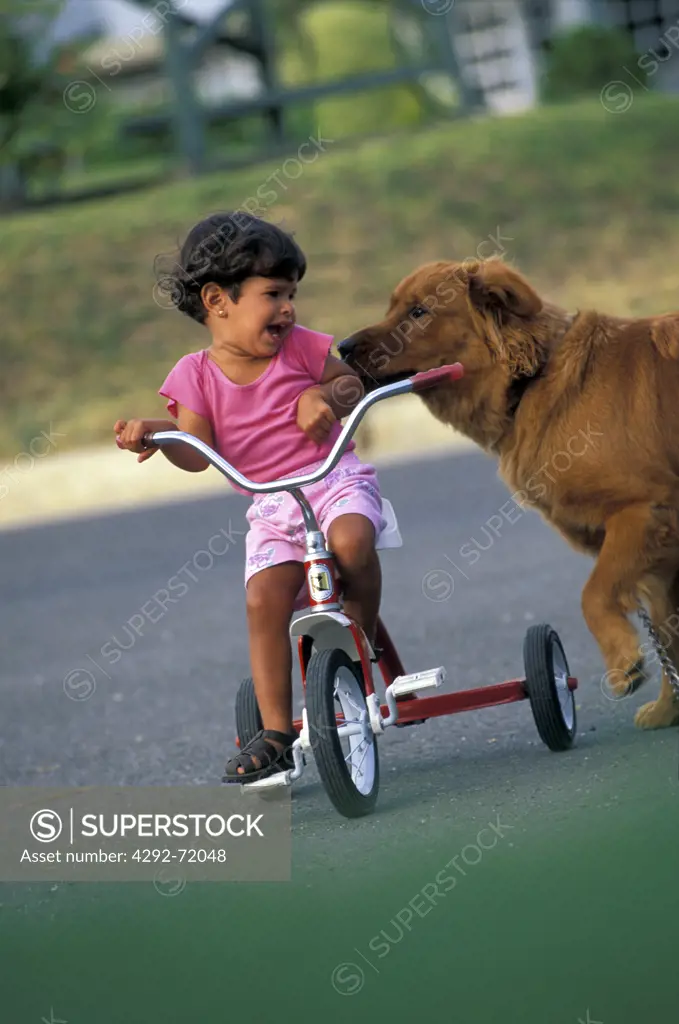 Girl on tricycle playing with dog