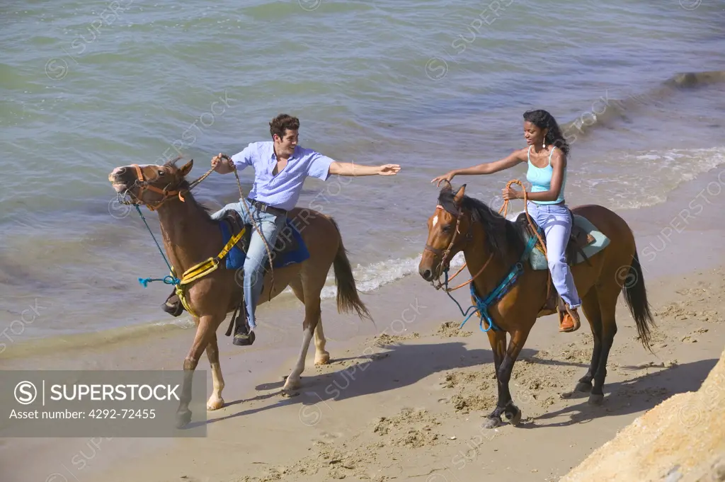 Couple riding horses along beach