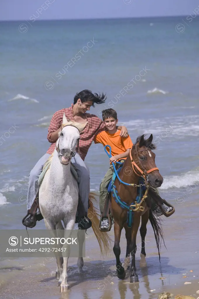 Father and son horseback riding on beach